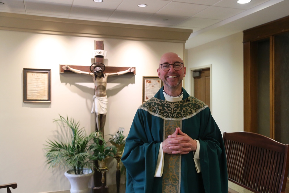 Priest in green vestments standing next to crucifix